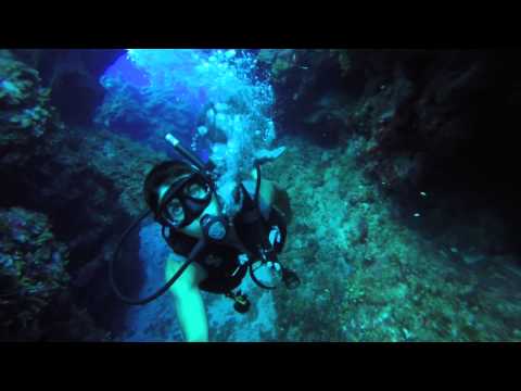 Scuba diver in full gear exploring an underwater cave with blue light and coral walls.